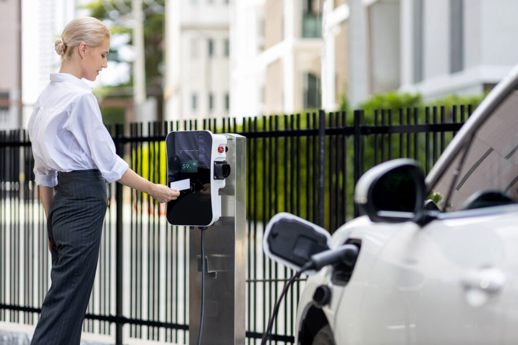 Credit card payment for eco-friendly clean and sustainable energy for electric vehicle at charging station. Progressive woman pay for charging point to power her electric rechargeable vehicle.